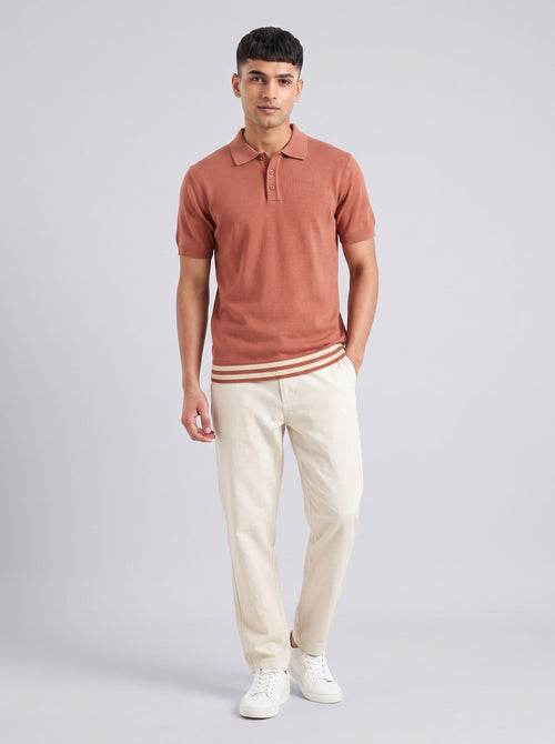 Model wearing The Awning terracotta knit polo with a cream and rust striped hem, with cream trousers