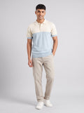 Model wearing The Deck Chair colourblock knit polo with an ecru yoke and pale blue body, with stone trousers