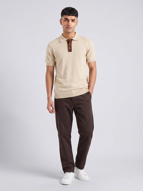 Model wearing The Interval ecru knit polo with a contrast brown placket, with dark brown trousers