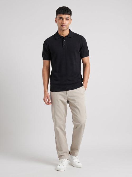 Model wearing The Last Train black knit polo with a three-button placket, with stone trousers