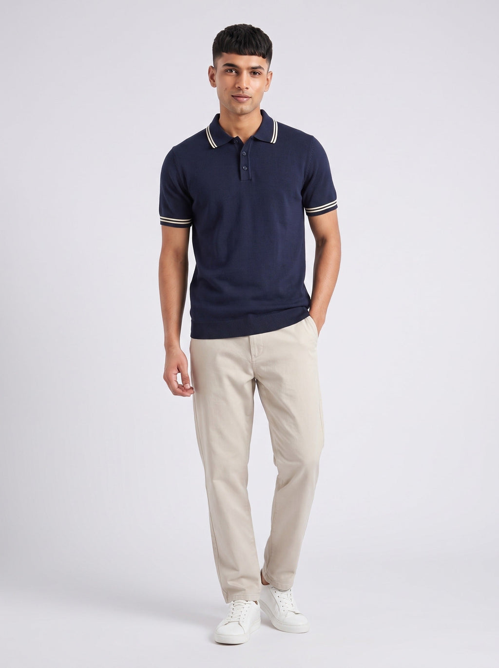 Model wearing The Pavilion navy knit polo with twin ecru tipping at the collar and cuffs, with stone trousers