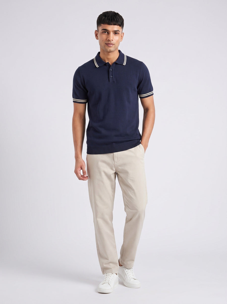 Model wearing The Pavilion navy knit polo with twin ecru tipping at the collar and cuffs, with stone trousers
